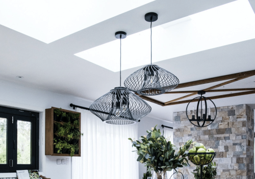 Modern kitchen with velux skylights, pendant lights, white cabinetry, and an island countertop. There are plants on the island and a stone accent wall in the background.