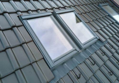 Closeup of attic window on house roof top covered with ceramic shingles. Tiled covering of building.