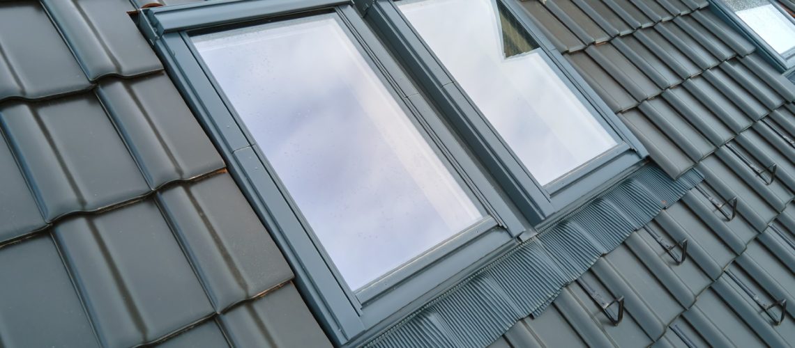 Closeup of attic window on house roof top covered with ceramic shingles. Tiled covering of building.