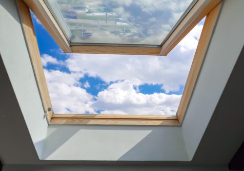 Looking on clouds flying past at the blue sky through open attic window in house roof.