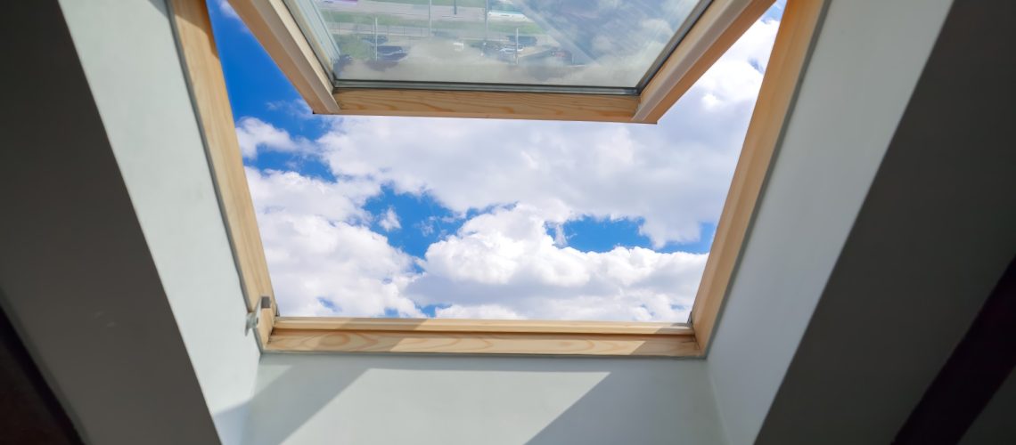 Looking on clouds flying past at the blue sky through open attic window in house roof.