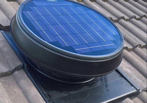 Circular solar panel installed on a tiled roof, housed in a black casing with integrated ventilation for optimal performance.