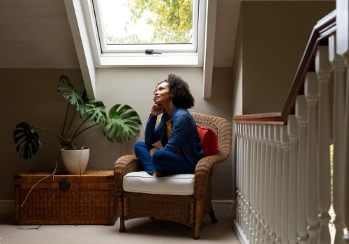 Thoughtful biracial woman looking out roof window at home. Relaxation, lifestyle and domestic life, unaltered.