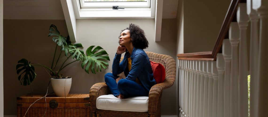 Thoughtful biracial woman looking out roof window at home. Relaxation, lifestyle and domestic life, unaltered.