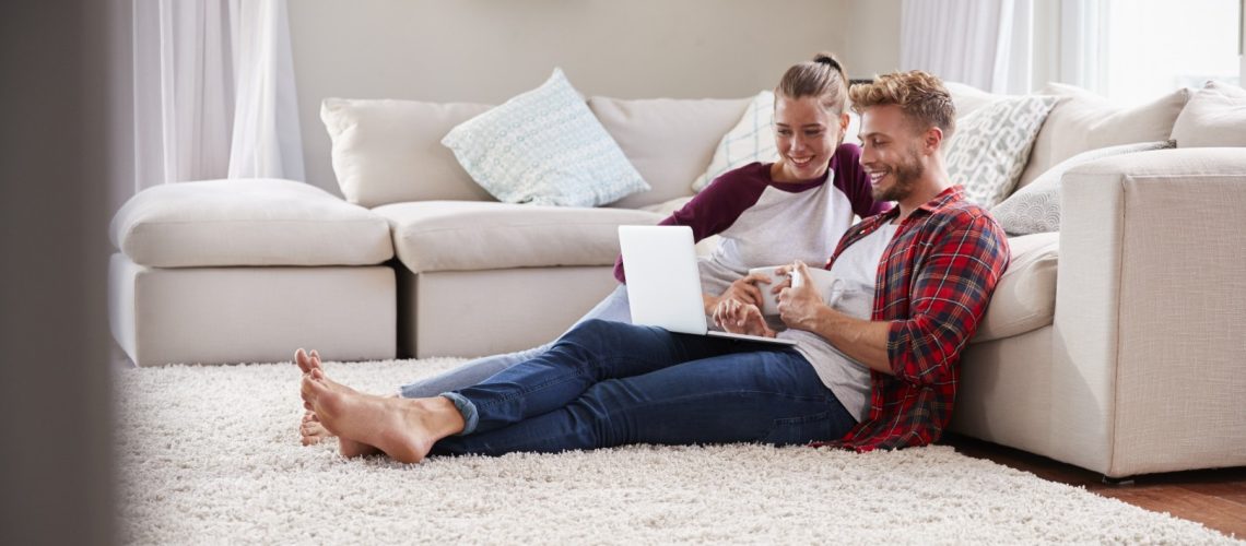 Young white couple sitting on the floor at home using laptop